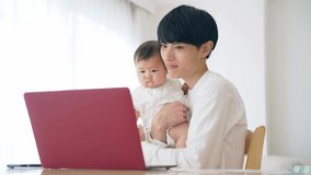 Young Asian man working at home with a baby. Remote work. Telework.