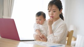 Young Asian woman working at home with a baby. Remote work. Telework.