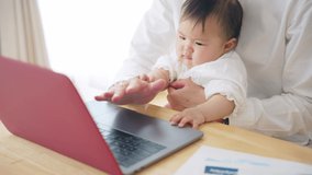 Young Asian man working at home with a baby. Remote work. Telework.