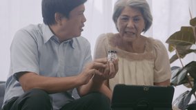 Asian of aged couple looking at screen of tablet and talking to doctor using online video call.