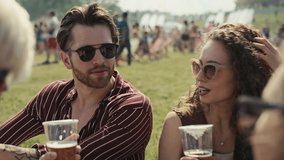 Group of friends sitting on grass together at music festival and drinking beer while chatting. Shot with RED helium camera in 8K.