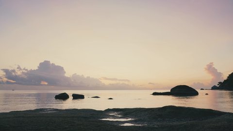 Man sitting on the rocky tropical beach and enjoying sunrise