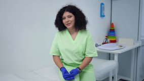Cheerful plus-size doctor talking smiling looking at camera sitting indoors. Portrait of charming positive Caucasian woman posing in hospital blogging. Lifestyle and health care concept