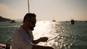 4K Confident Caucasian man enjoy luxury outdoor lifestyle drinking whiskey while catamaran boat sailing in the sea at summer sunset. Handsome guy relaxing on sail yacht on holiday travel vacation. - Powered by Shutterstock - Get 15% off with code: PIKWIZARD15