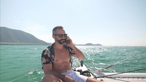 4K Caucasian businessman talking on mobile phone for corporate business while travel catamaran boat sailing in the sea. Handsome guy enjoy luxury outdoor lifestyle on sail yacht on summer vacation. - Powered by Shutterstock - Get 15% off with code: PIKWIZARD15