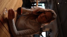 Vertical portrait of beautiful blonde young woman sitting in restaurant alone, talking on mobile phone and drinking red wine. Sad pretty lady in bar drinking wine and talking on smartphone. - Powered by Shutterstock - Get 15% off with code: PIKWIZARD15