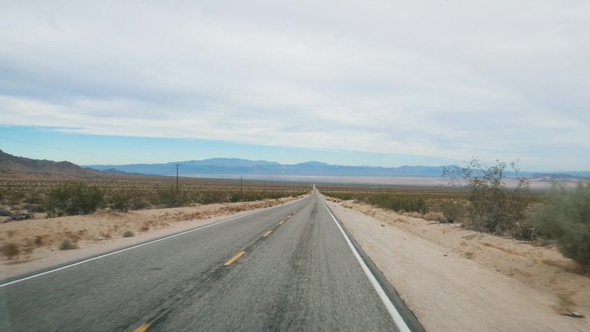 Driving on empty asphalt straight road going to horizon of hilly mountains and passing through desert in Death Valley in western Usa. Aerial flying forward. Traveling by car through national parks