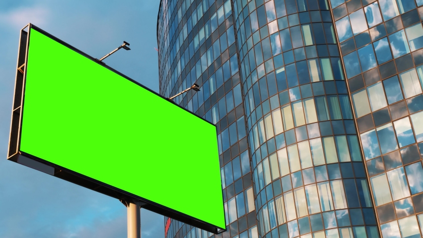 Advertising billboard green screen chroma key against a glass office modern building and a blue sky with moving clouds, time lapse. Mock up concept. . High quality 4k footage