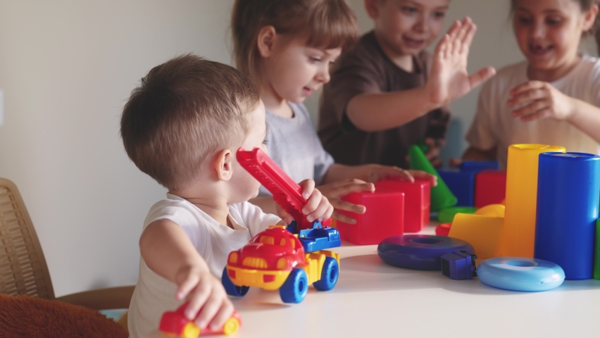 Kids girl and baby boy play in kindergarten. a group of children play toys cubes and cars on the table in kindergarten. happy family preschool education indoor concept. nursery baby toddler home