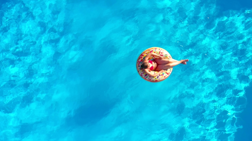 Aerial view of a woman in red swimsuit lying on a donut in the pool