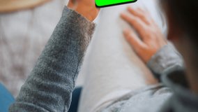 Woman at home using smartphone with green mock-up screen in vertical mode. Girl browsing Internet, watching content, videos