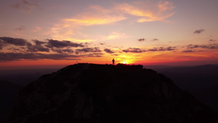Silhouette of a person on top of a mountain at sunset, Colorfull clouds sky. 4K aerial drone view. 