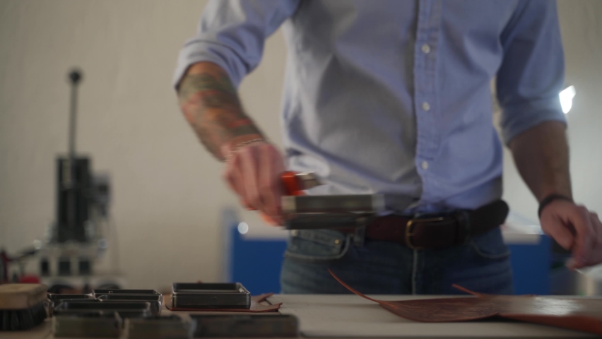 Leather craftsman works in his workshop. Master making leather products. Man carves leather sheet shape for die punch cutter leather punching knife. Male fits on craft cutting mold.
