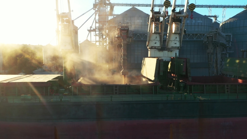 Aerial view fom above - wheat loading to bulker ship cargo hold at sea grain elevator in sea port. Wheat shipment from silo to vessel via moving trunk at a sea port terminal. Maritime transport. Royalty-Free Stock Footage #1092184293