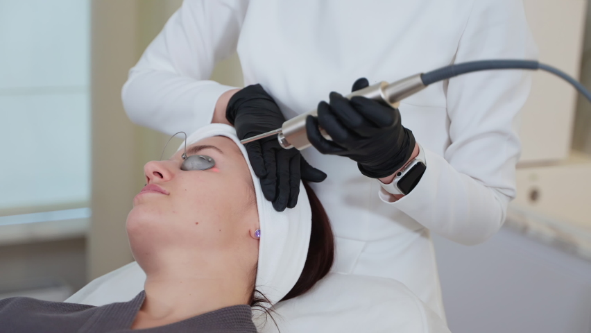 Woman at beauty salon. She receiving facial treatment with professional cosmetology equipment. Skin therapy with YAG laser | Shutterstock HD Video #1092185983