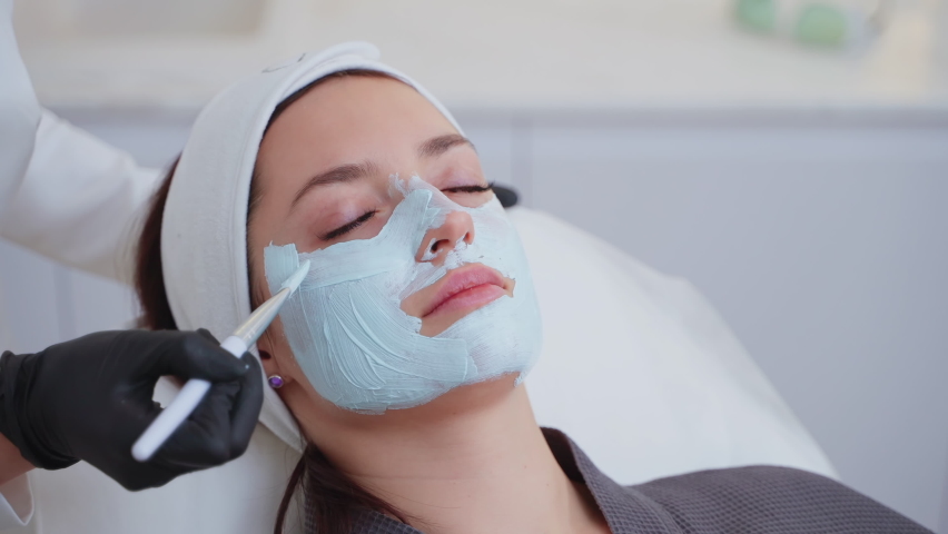 Close-up shot of a woman enjoying facial treatment with clay mask at beauty shop. Cosmetology and spa