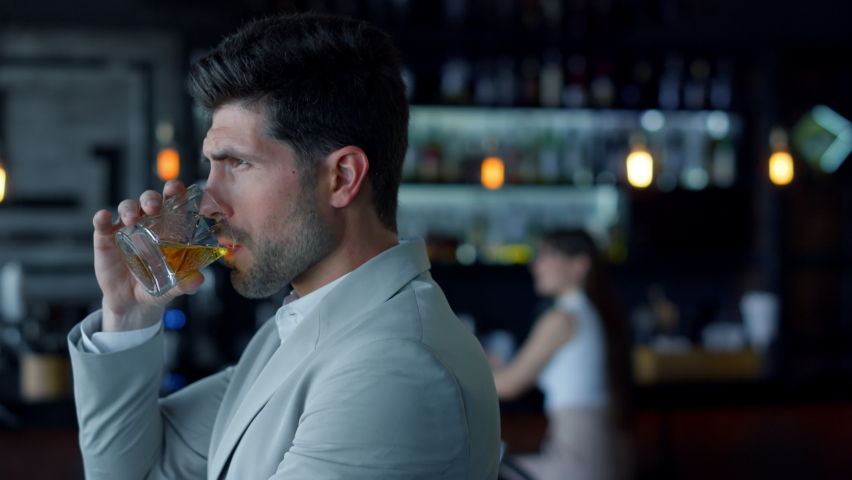 Leader person drinking whiskey in restaurant. Handsome thoughtful gentleman tasting beverage in luxury cafe. Businessman holding bourbon glass and relaxing. Unknown woman silhouette background
