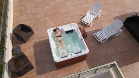 Slowmotion video. Aerial shot of a young woman relaxes in the hot tub on a rooftop