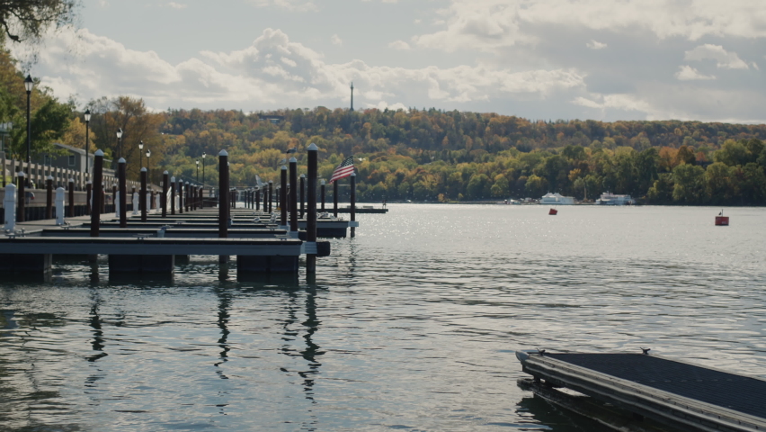 A woman stands on a pier overlooking Lake Ontario, the American flag is visible in the distance, there are no other people and yachts around. Autumn and end of tourist season.