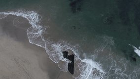 Aerial drone video of waves breaking against the rocks on the shore. Top view footage