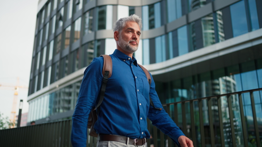 Successful happy businessman with backpack commuting in city street sunny day.