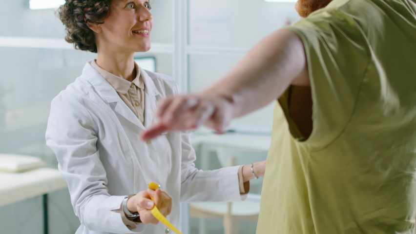 Tilt up shot of female doctor measuring waist of male patient with obesity while giving him health checkup in clinic