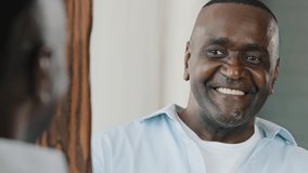 Close up portrait mirror reflection happy senior retired african adult american man with bristle smiling wink himself stand in dressing room planning date makes thumb up hand gesture feels confidence - Powered by Shutterstock - Get 15% off with code: PIKWIZARD15