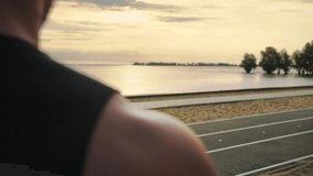 Muscular man in a T-shirt stands watching the sunset on the beach.Slow Motion.