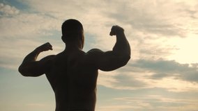 Bodybuilder poses with his back to the camera. Back Double biceps on the sunrise.Slow Motion