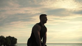 Bodybuilder is training outdoors, throwing kettlebells in front on sunrise. Slow Motion