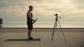 Athletic man training outdoors, recording online classes, doing lunges with weights filmed it on camera