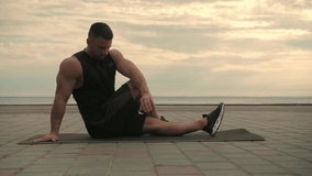 Athletic man training outdoors, doing stretching exercises against a background of the sea and open sky