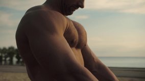 Athletic man flexing his chest muscles against the beautiful sunrise. Blue sky in the frame
