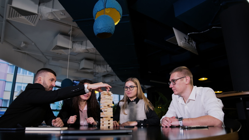 Four adults play table games sitting in the cafй. People playing jenga, laughing, having great time together.