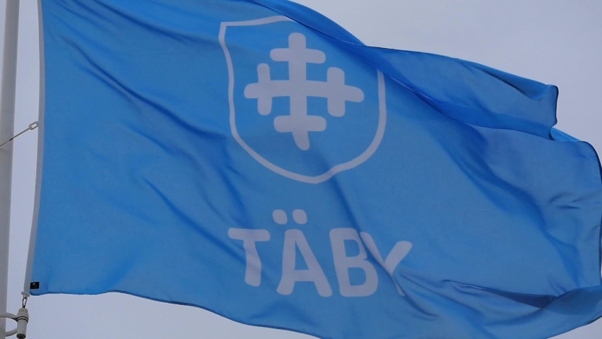Blue flag with the Täby municipality (kommun) logotype on it. Waving peacefully in slow motion, with a grey sky behind it. Swedish governance and local politics concept. Royalty-Free Stock Footage #1092223215