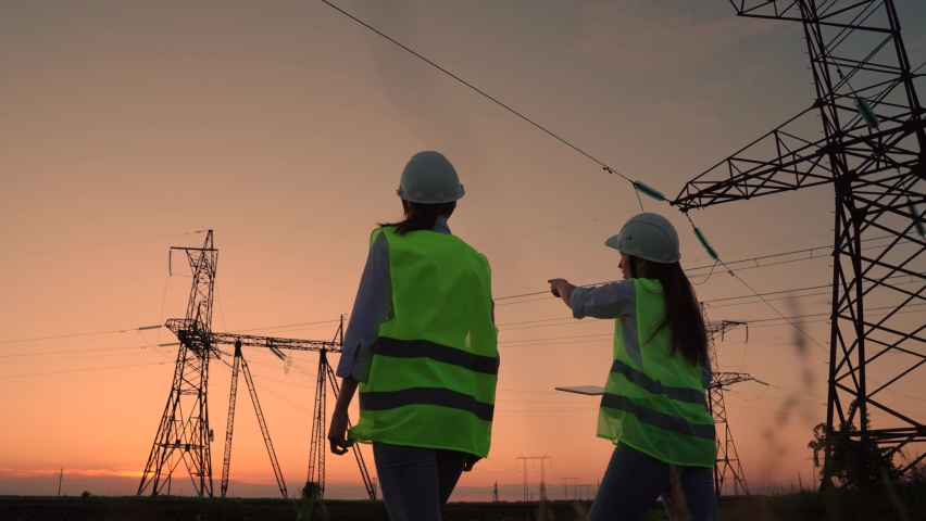 Two civil engineers work together using computer tablet on a power line. Joint work of power engineers with computer in protective helmets, maintenance of power lines in outdoors. Green energy | Shutterstock HD Video #1092224355