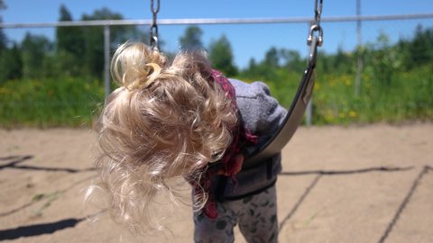 Close up slow mo clip of a cute three year old child lying on stomach over a playground swing and swaying backwards and forwards. Copy space to sides.