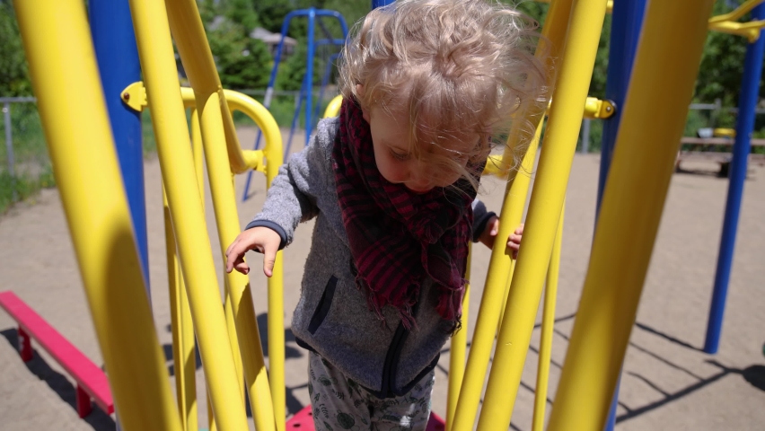 Close up front video in slow mo, as inquisitive three year old caucasian boy is seen exploring the climbing frame and kids apparatus at local park. Royalty-Free Stock Footage #1092229549
