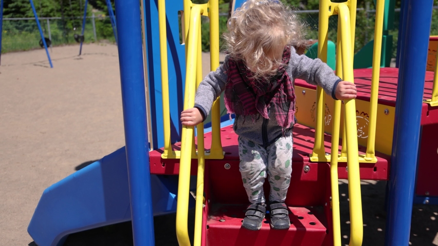 Slow mo video of a two year old caucasian boy jumping from the stairs of a playground slide, accidentally slipping and landing seated on bottom step. Royalty-Free Stock Footage #1092229557