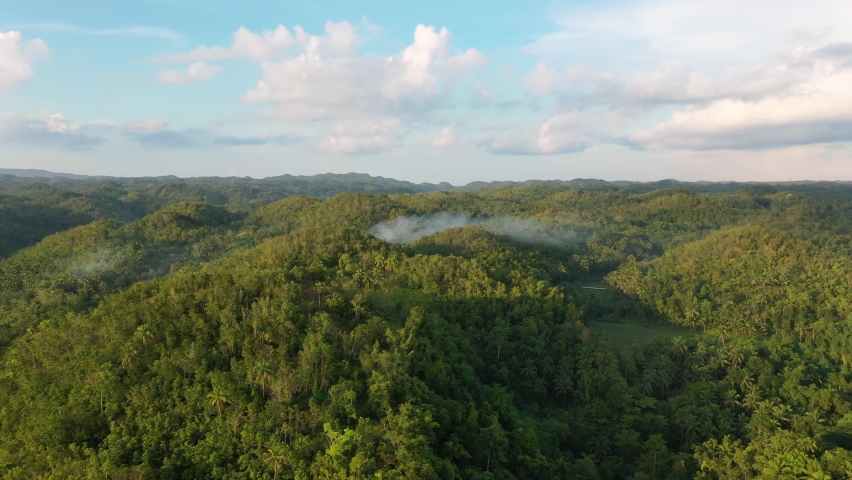 Short movie over a tropical rainforest in South East Asia, with low lying patches of fog at treetop level beneath a blue sky and scattered clouds. Royalty-Free Stock Footage #1092229595