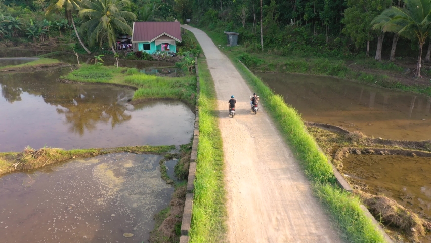 Drone footage following two mopeds driving on a country road in small village in the Philippines with traditional house and bridge over paddy fields. Royalty-Free Stock Footage #1092229639