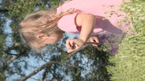 VERTICAL VIDEO: Little girl tries to catch butterfly on butterfly net in city park. Cute little girl catching butterfly on aerial insect net in meadow on sun day. Slow motion