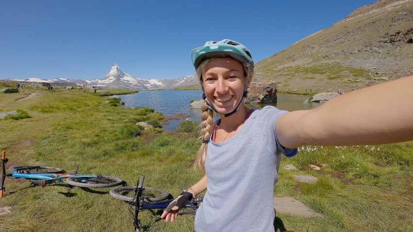 Female mountain biker takes cool selfie near trail in the mountains. Matterhorn peak in Zermatt. 