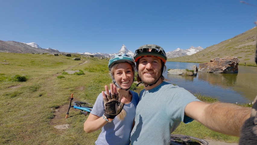 Happy couple taking selfie photo while enjoying mountain biking in summer. People doing sport activities in nature taking selfie. Matterhorn mountain, Zermatt 