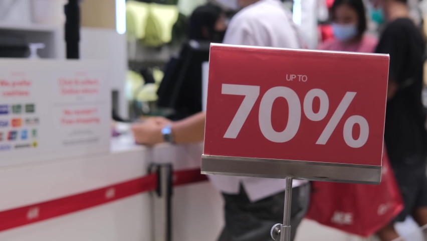 Red sign with a 70 percent discount to attract customers. In the background in blur, unrecognizable customers at the checkout are eager to buy at a bargain price in the store. Discount concept. Royalty-Free Stock Footage #1092234079