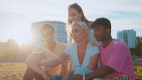 Young multi-ethnic hipster best friends on summer video chatting using smartphone at a beach. Four young multiracial people spending time together. Friendship, communication, youth a lifestyle concept
