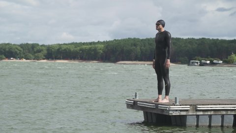 Pro swimmer, triathlete in wetsuit for swims walks along the pier and prepares to jump into the water, training day, preparation for triathlon.