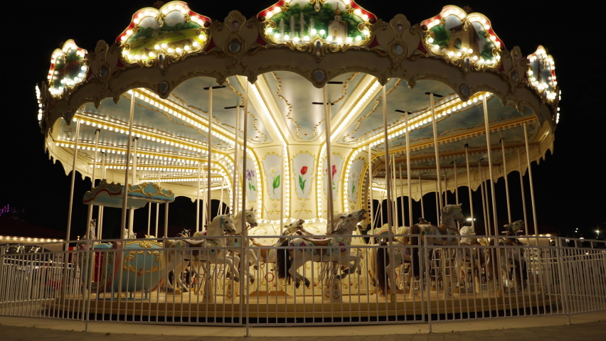 Illuminated children's vintage carousel and horses. Rotation of the carousel in the evening in the park. Royalty-Free Stock Footage #1092242631