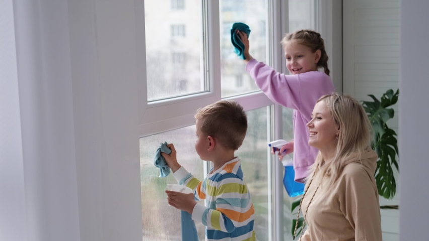 Happy family washes the window. Mom,daughter and son do house cleaning. Mother teaches children to clean windows. Royalty-Free Stock Footage #1092246037