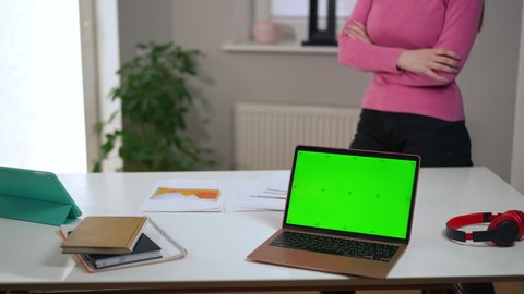 Unrecognizable troubled woman walking side to side in home office with green screen laptop on table. Worried anxious startuper freelancer thinking planning e-business indoors. Intelligence concept